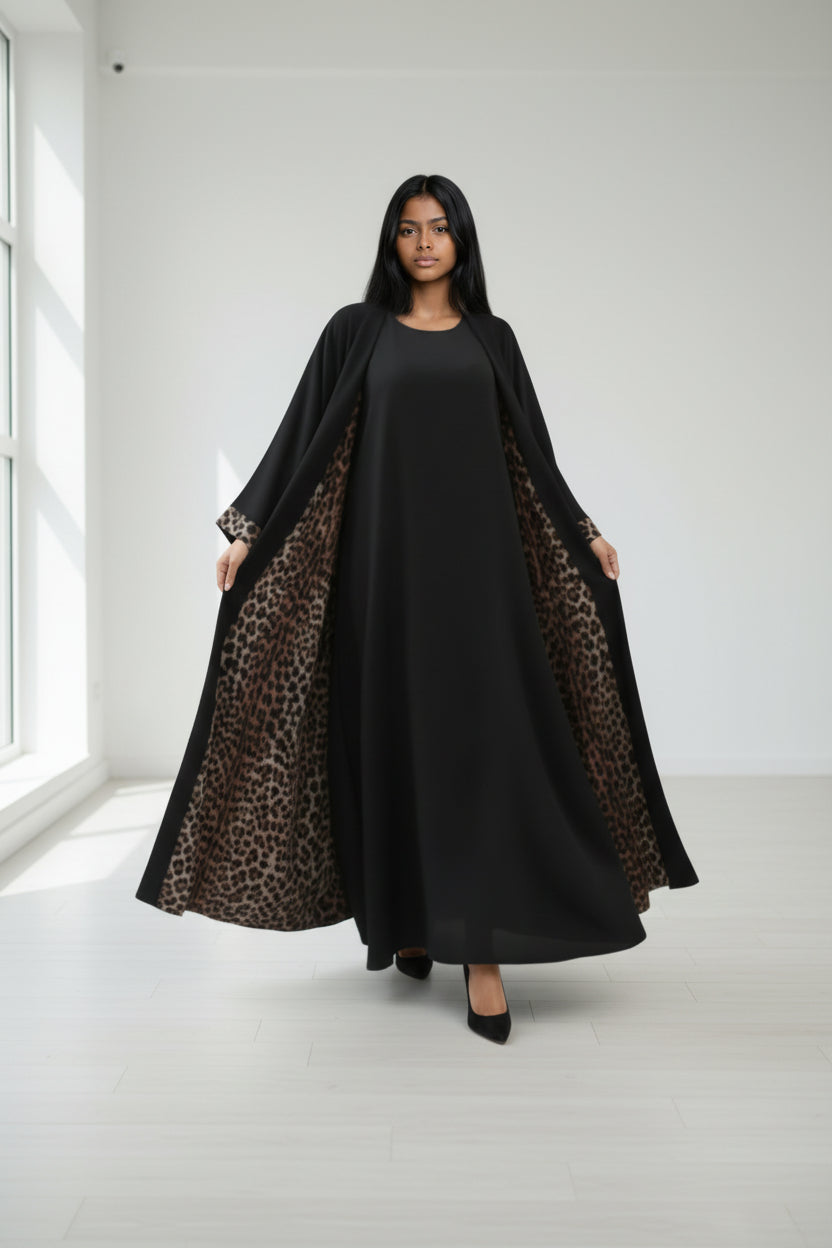 Woman wearing a black dress with leopard print sleeves in a white room.