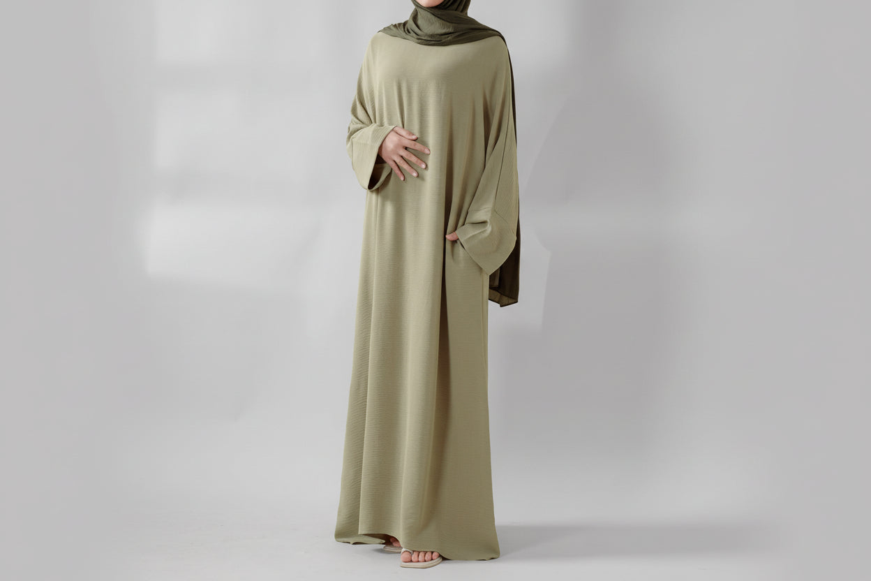 Person wearing a long, light-colored dress with a hijab on a beige background