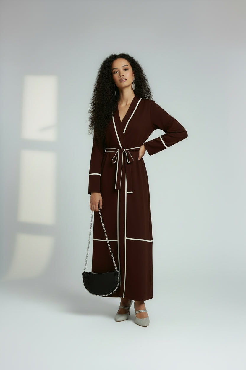 Woman wearing a brown robe with white trim, holding a black handbag on a white background