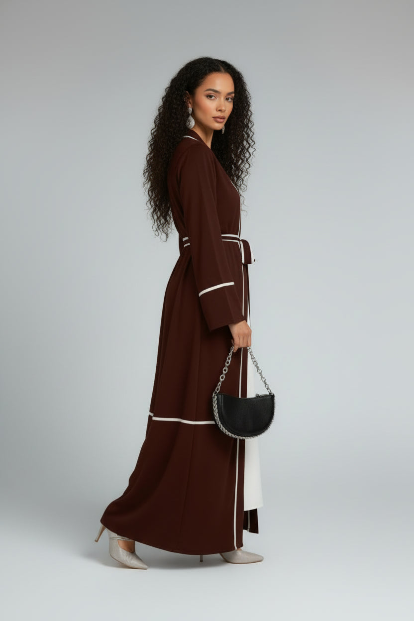 Woman wearing a brown dress with white trim, holding a black handbag on a gray background
