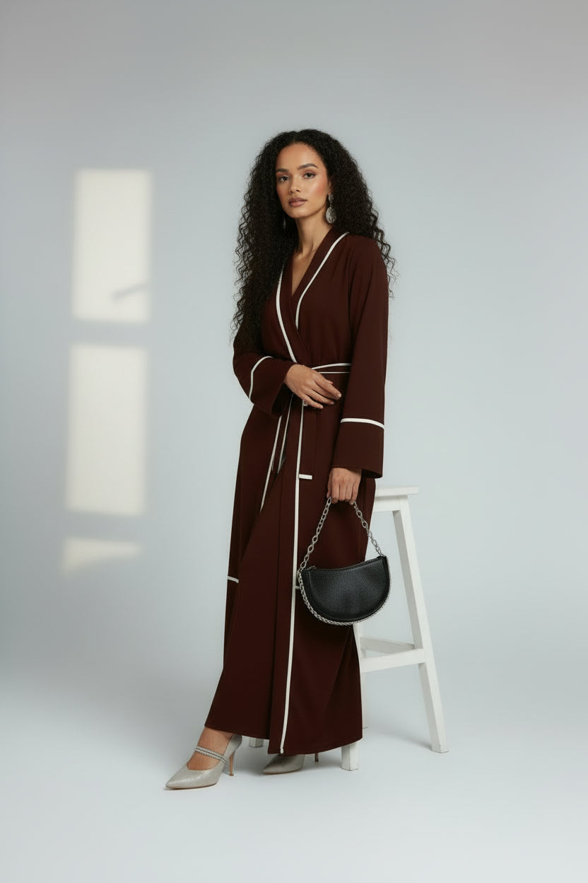Woman in a long brown robe holding a black handbag on a white background